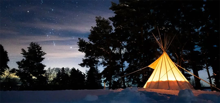 Ett tält lyser i skymningsmörkret mot en stjärnklar vinterhimmel